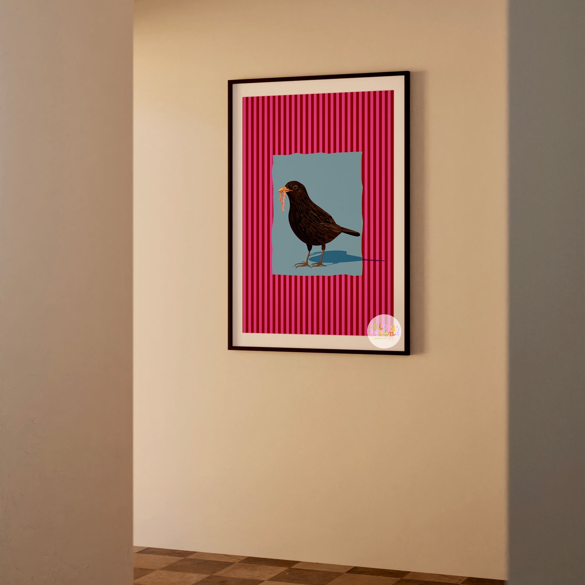 pink and blue bird-inspired wall art. Wall art with a vibrant striped pink background and a soft blue geometric square sits behind an original hand illustration of a blackbird with a worm in its mouth. Colourful, bold dopamine decor art print for nature lovers displayed in a wood frame