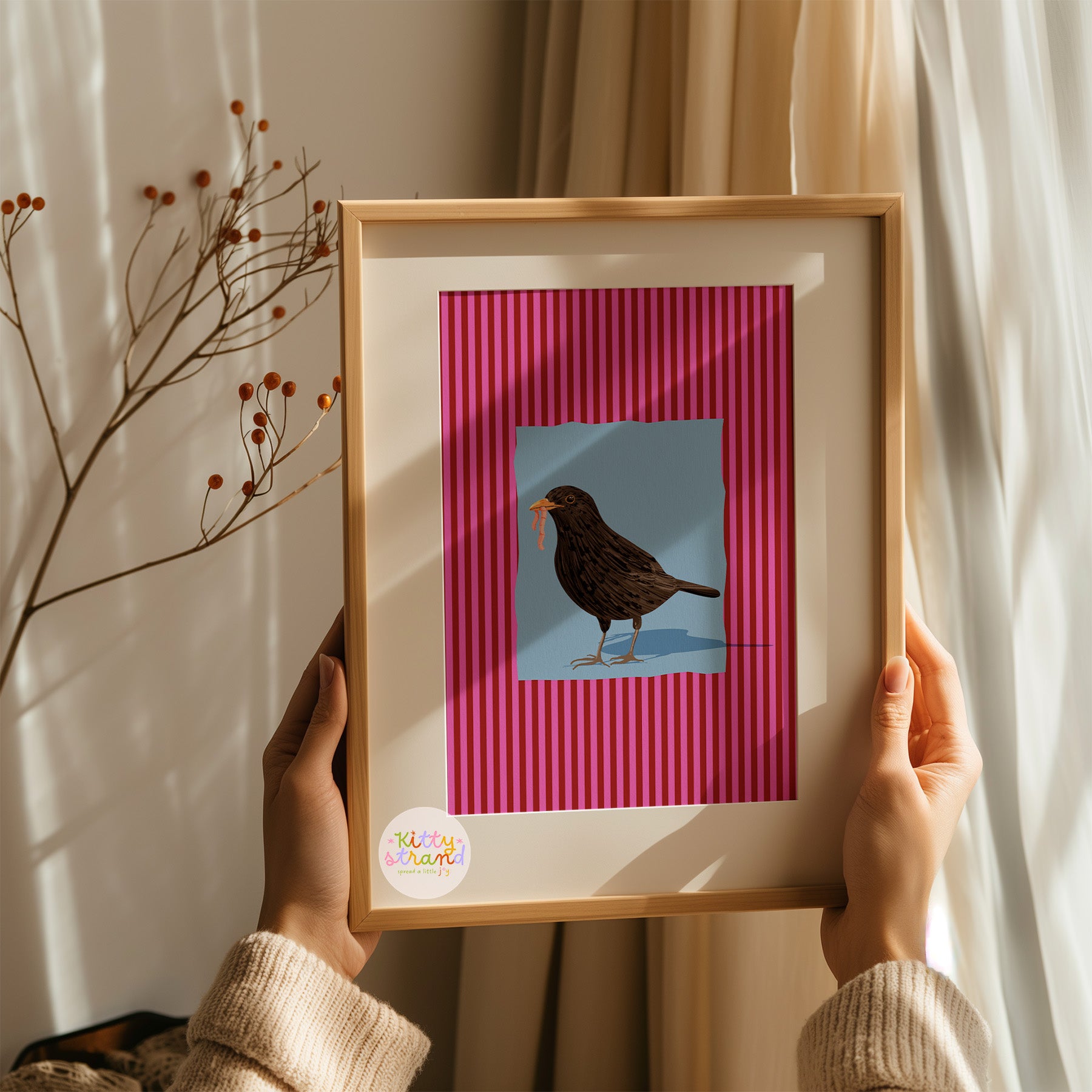 pink and blue bird-inspired wall art. Wall art with a vibrant striped pink background and a soft blue geometric square sits behind an original hand illustration of a blackbird with a worm in its mouth. Colourful, bold dopamine decor art print for nature lovers displayed in a wood frame