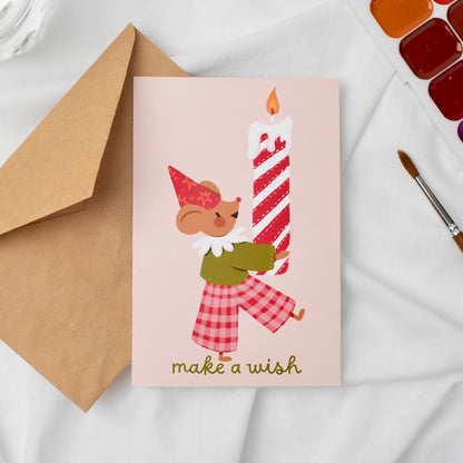 Greeting card with a Mouse holding a candy cane candle and 'make a wish' text, next to an envelope on a light background.