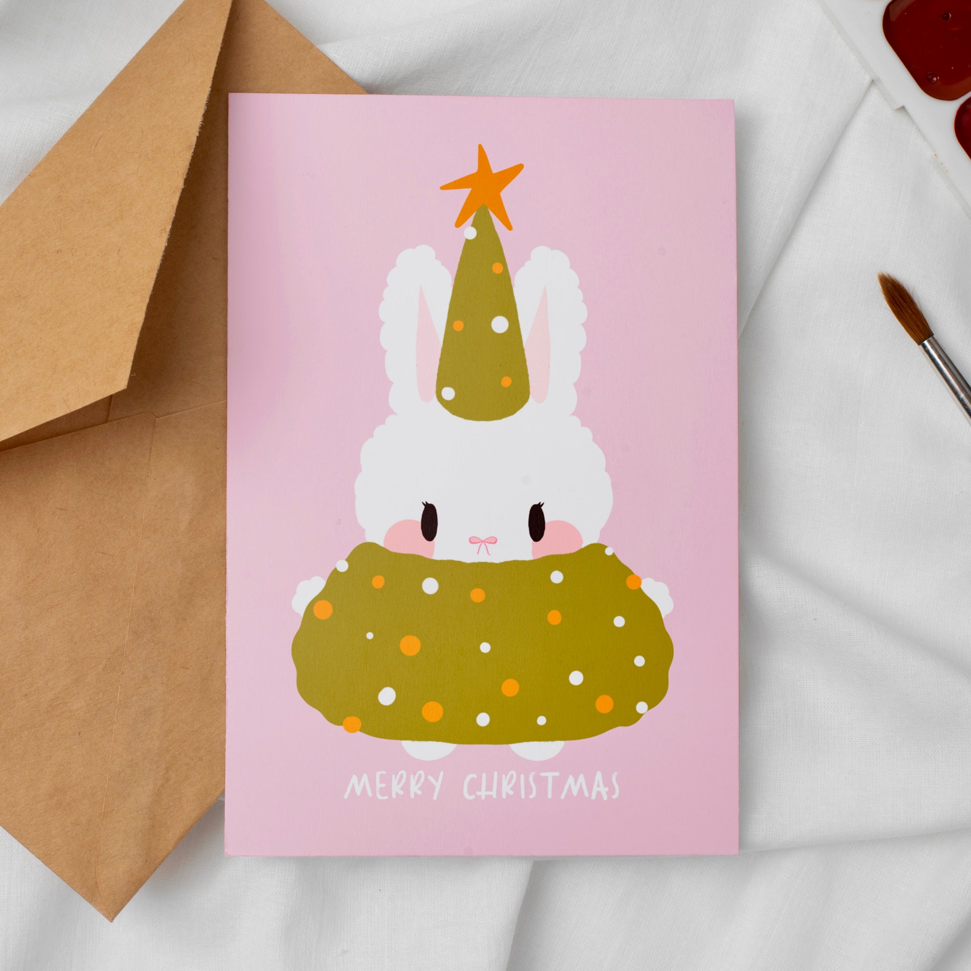 Greeting card with a festive bunny design on a pink background, accompanied by a brown envelope.