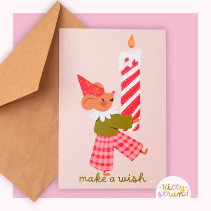 Greeting card with a Mouse holding a candle and 'make a wish' text, accompanied by a brown envelope on a pink background.