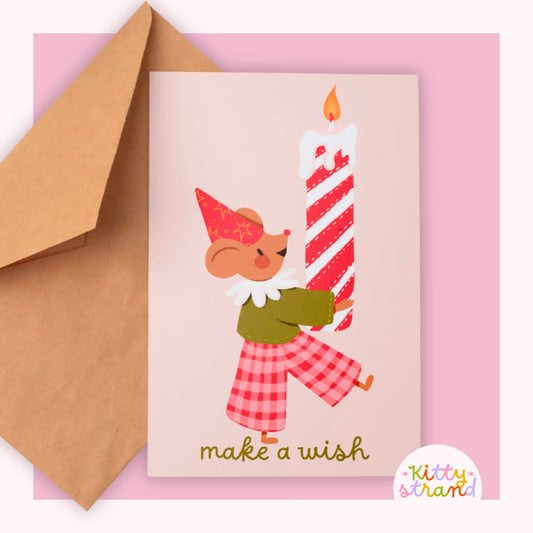 Greeting card with a Mouse holding a candle and 'make a wish' text, accompanied by a brown envelope on a pink background.