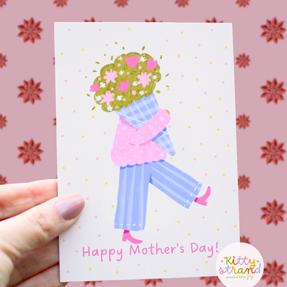 Mother's Day card with a stylized illustration of a woman holding flowers, held by a hand against a floral-patterned background.