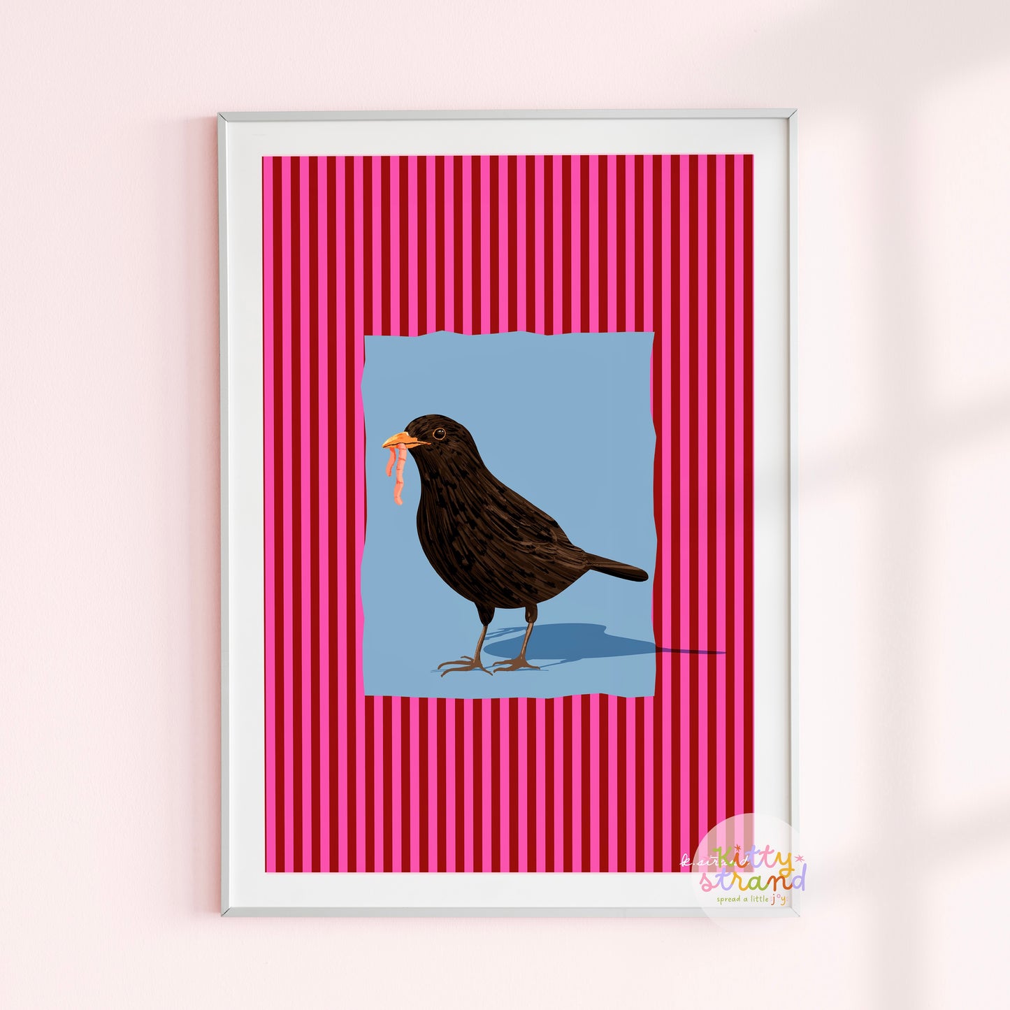 pink and blue bird-inspired wall art. Wall art with a vibrant striped pink background and a soft blue geometric square sits behind an original hand illustration of a blackbird with a worm in its mouth. Colourful, bold dopamine decor art print for nature lovers displayed in a wood frame