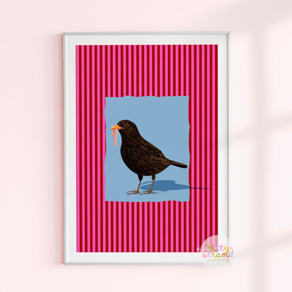 pink and blue bird-inspired wall art. Wall art with a vibrant striped pink background and a soft blue geometric square sits behind an original hand illustration of a blackbird with a worm in its mouth. Colourful, bold dopamine decor art print for nature lovers displayed in a wood frame