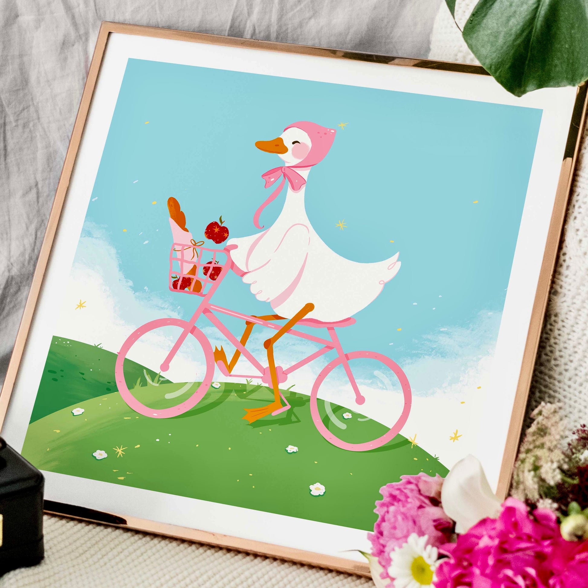 Framed illustration of a duck riding a pink bicycle with flowers and a basket.