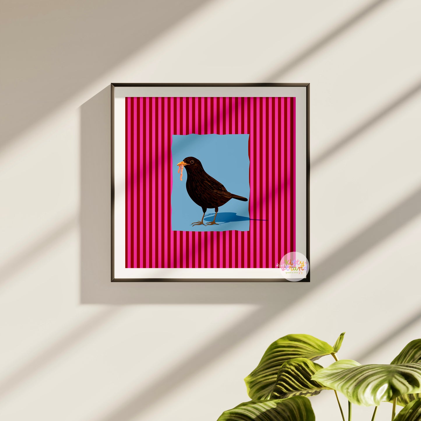pink and blue bird-inspired wall art. Wall art with a vibrant striped pink background and a soft blue geometric square sits behind an original hand illustration of a blackbird with a worm in its mouth. Colourful, bold dopamine decor art print for nature lovers displayed in a wood frame