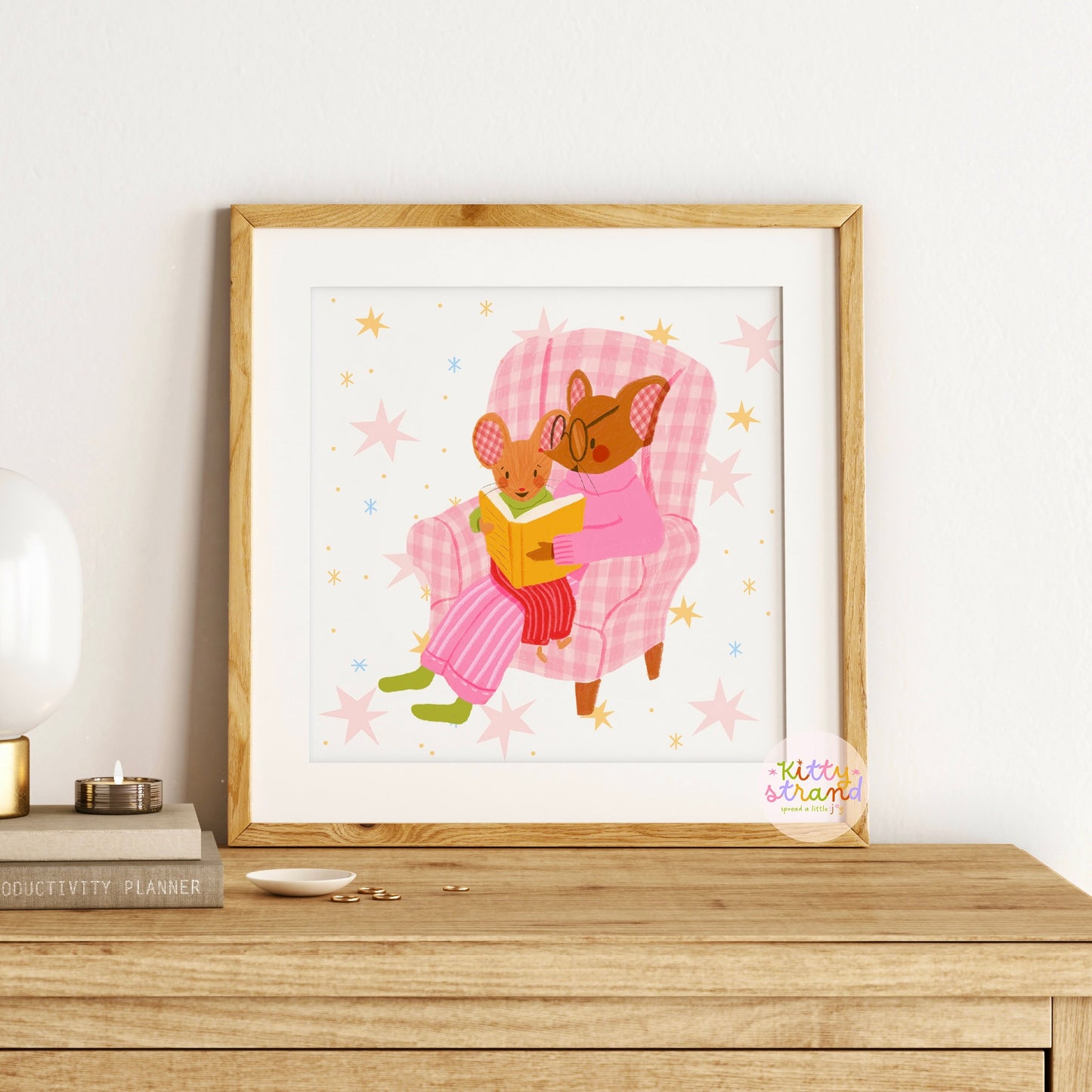 wall art with an illustration of two mice reading a book in a checkered chair with a pink background. Children's book inspired wall decor