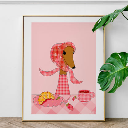 Framed artwork of a dog in a plaid outfit with a pink background, placed on a wooden surface with a plant in the corner.
