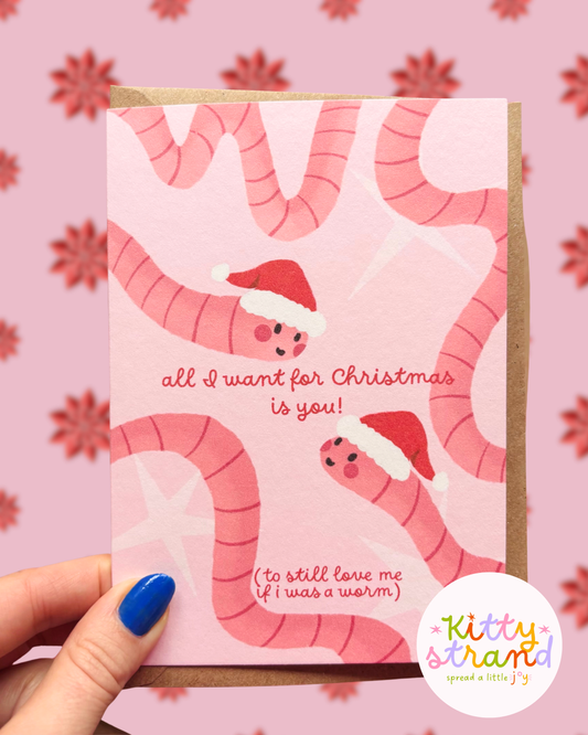 Christmas card for boyfriend with pink worms wearing Santa hats and text on a pink background. Text reads "All I want for christmas is you (to still love me if I was a worm)"