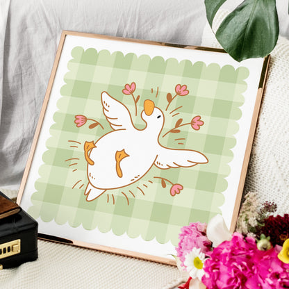 Framed illustration of a bird with flowers on a green checkered background, placed on a surface with flowers and a suitcase.
