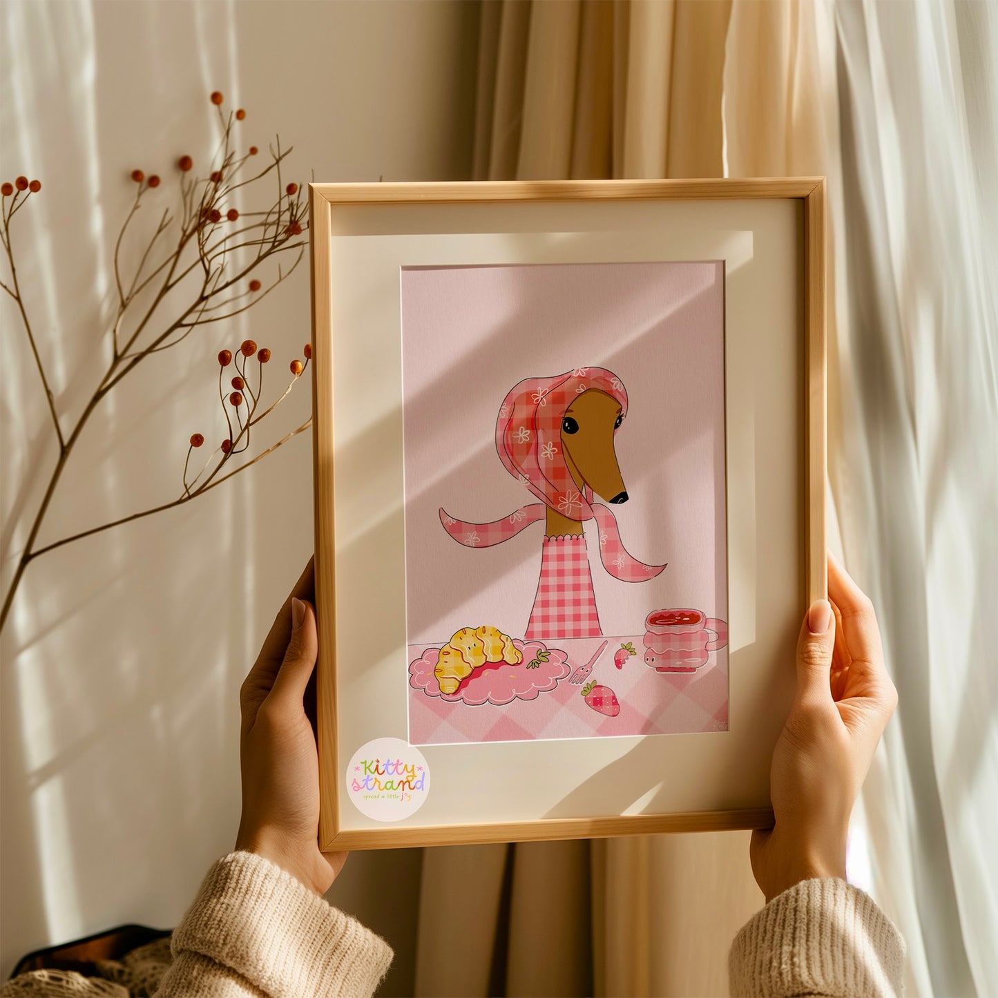Framed illustration of a dog with a pink checkered jumper and headscarf, held by a woman in a wooden frame