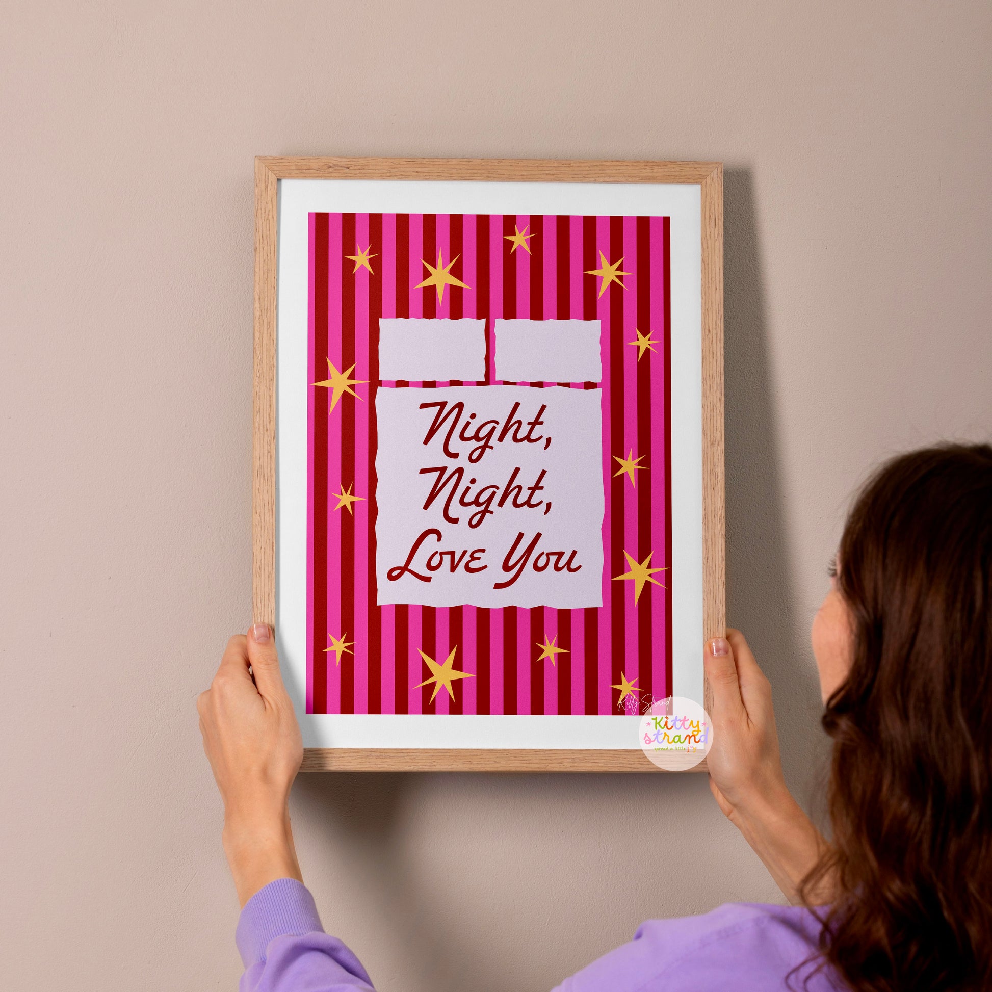 Person hanging a framed print with 'Night, Night, Love You' text on a wall.