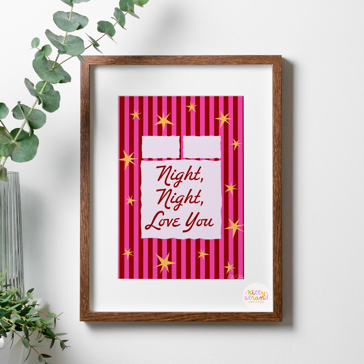 Framed artwork with 'Night, Night, Love You' text on a pink striped background, placed on a white surface with a plant.