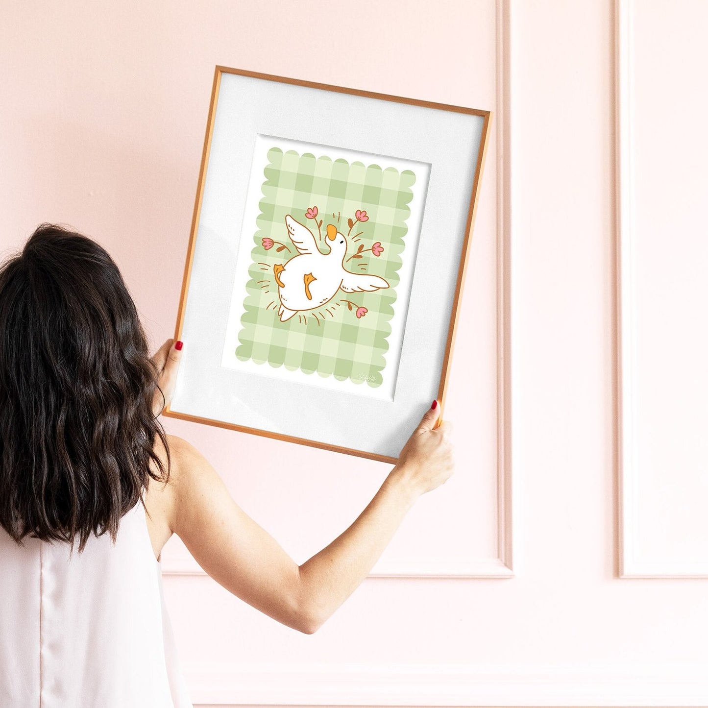 Person holding a framed illustration of a goose on a pink wall