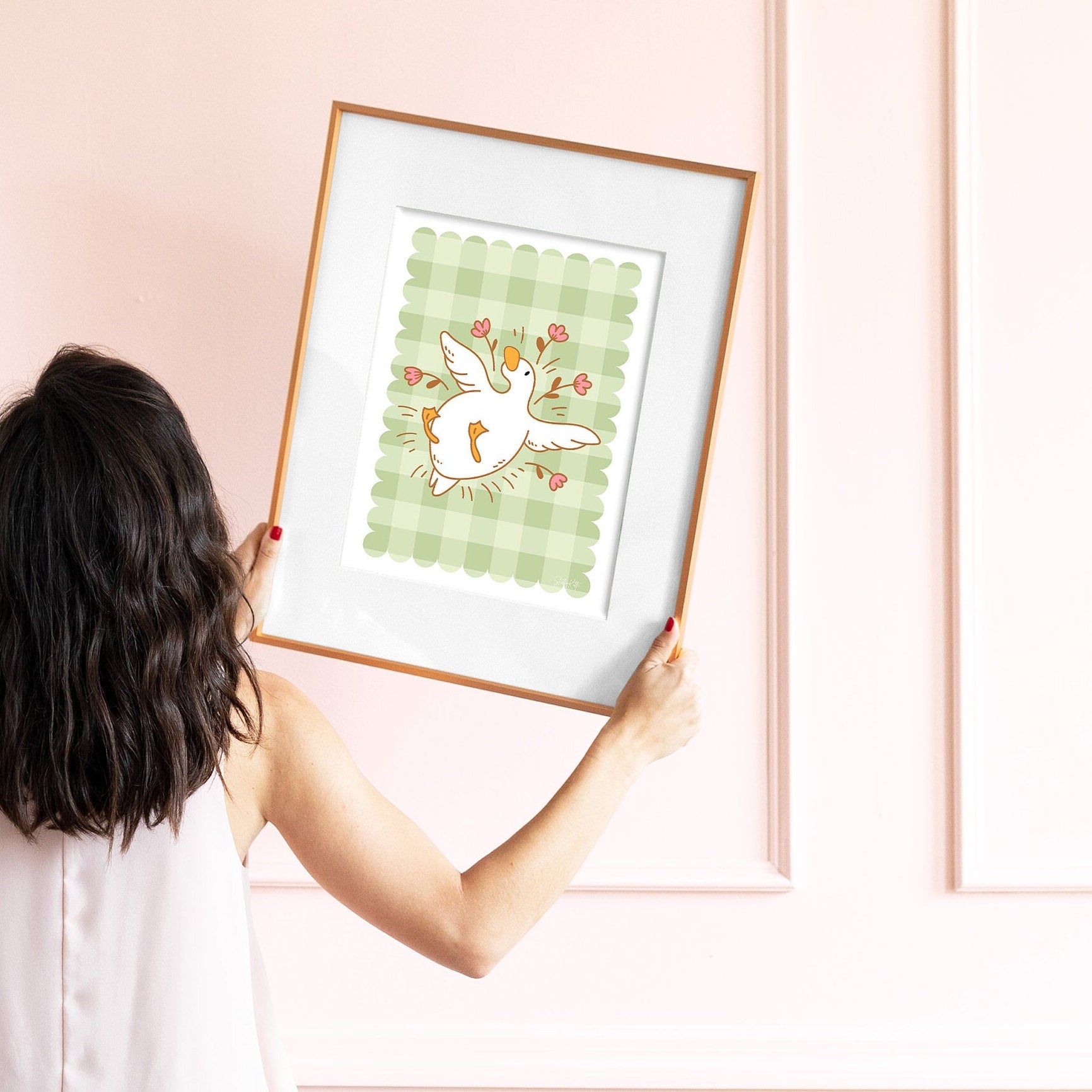 Person holding a framed illustration of a goose on a pink wall