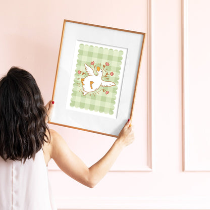 Person holding a framed illustration of a goose on a pink wall