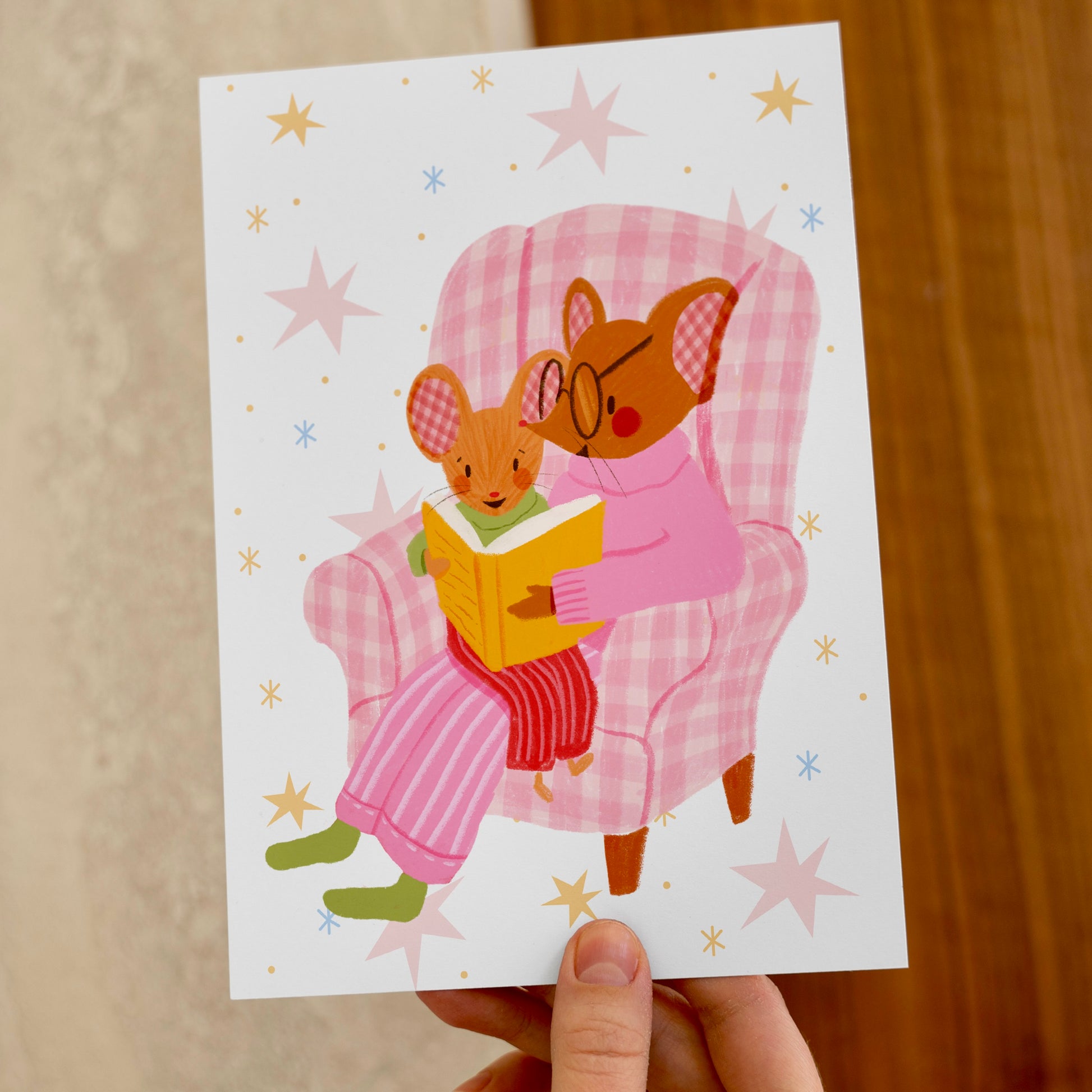 wall art with an illustration of two mice reading a book in a checkered chair with a pink background. Children's book inspired wall decor