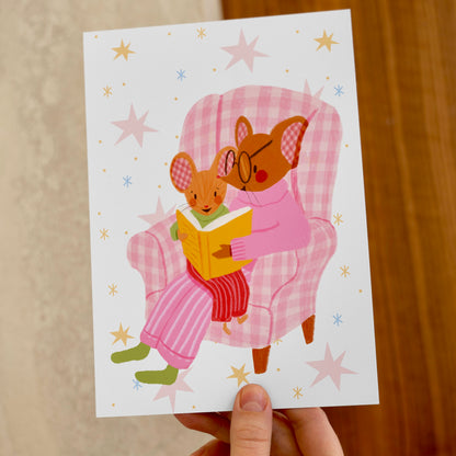 wall art with an illustration of two mice reading a book in a checkered chair with a pink background. Children's book inspired wall decor