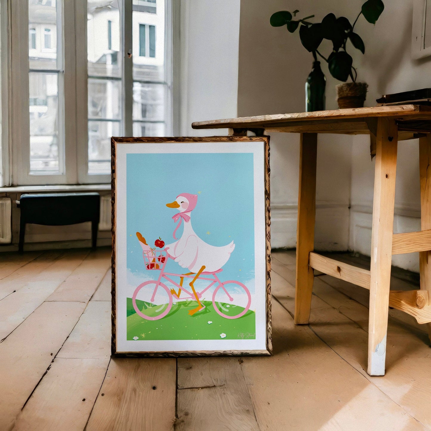 Framed illustration of a duck riding a bicycle on a wooden floor.