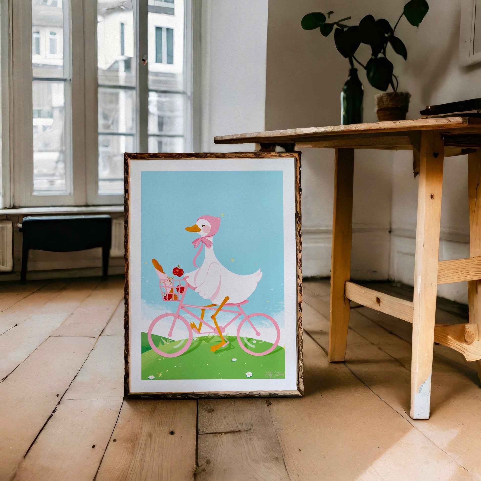 Framed illustration of a duck riding a bicycle on a wooden floor.