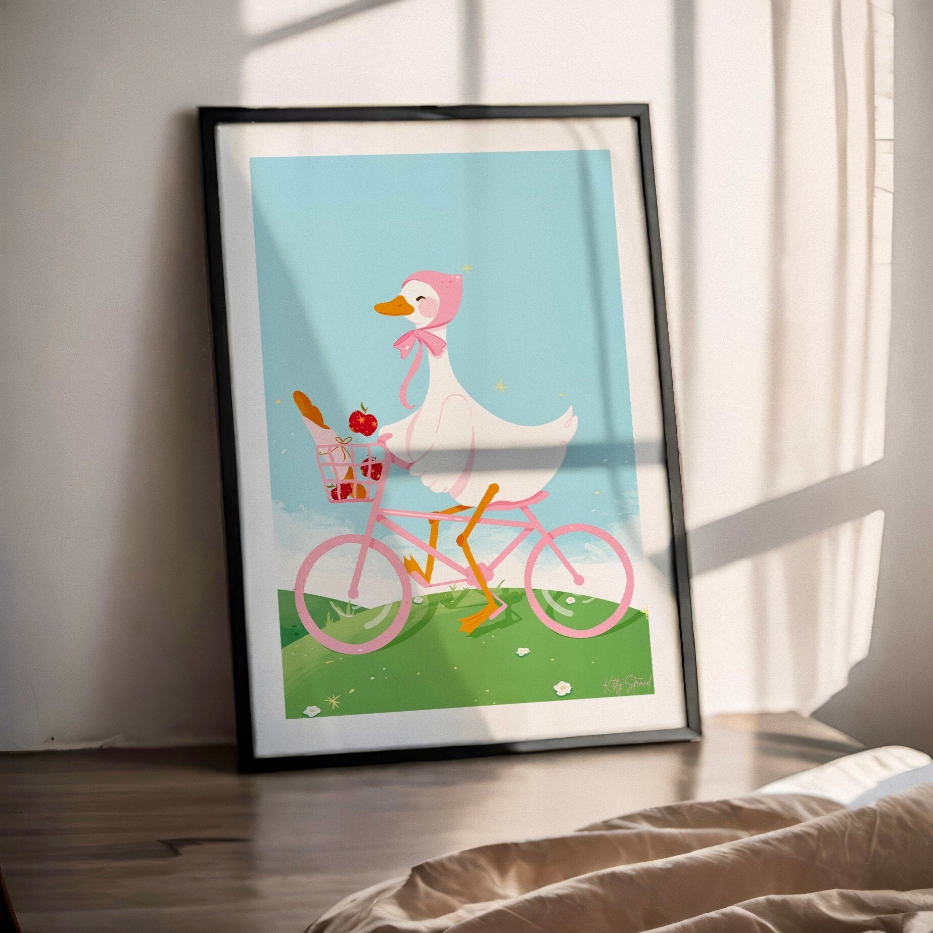 Framed artwork of a cartoon duck riding a pink bicycle indoors.