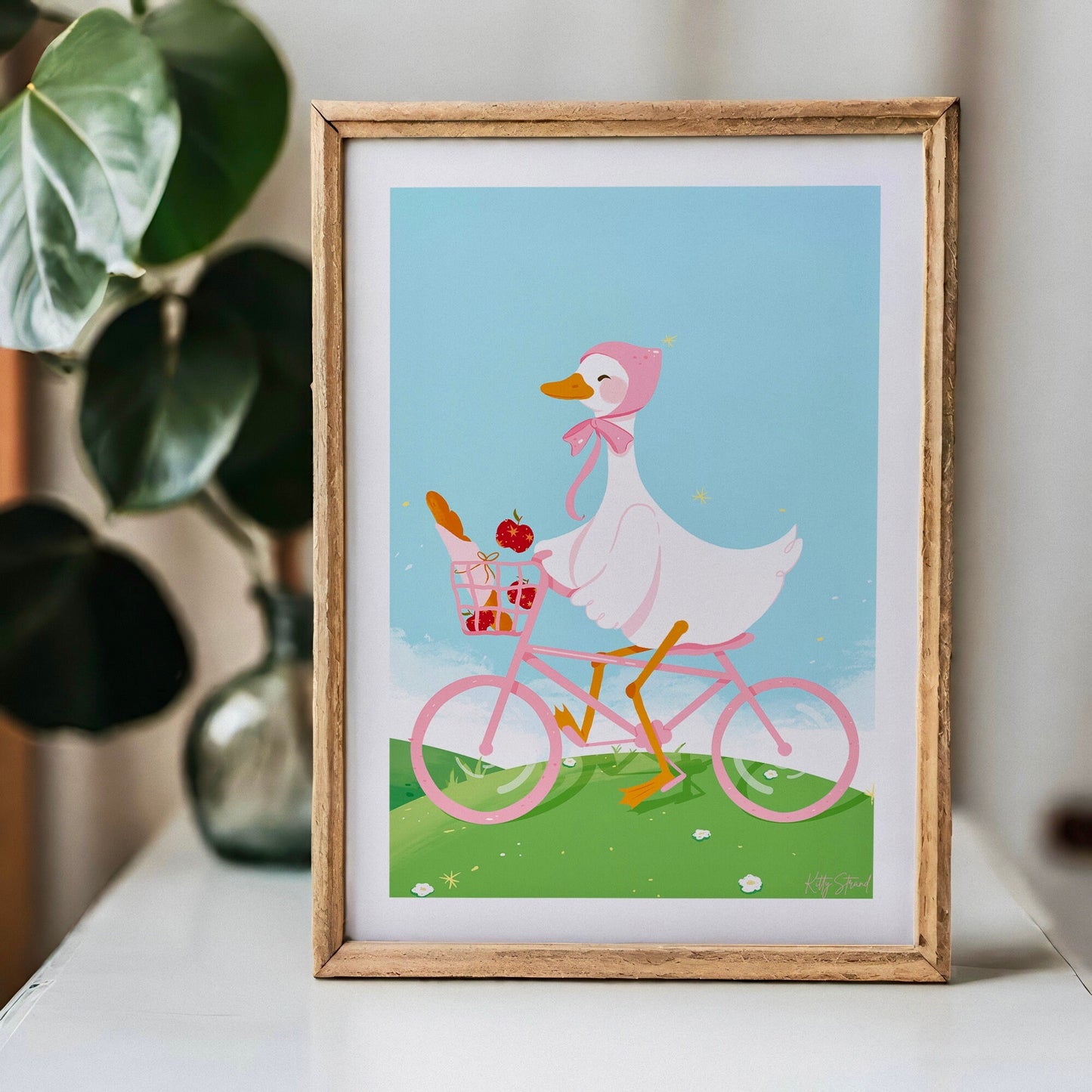 Framed illustration of a duck riding a pink bicycle with a plant in the background